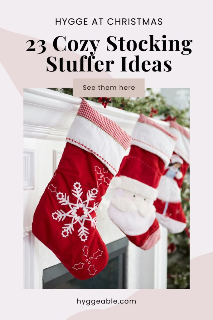 Three red and white Christmas stockings with festive patterns hang from a white mantelpiece, topped with greenery and holiday decor. Text reads, 23 Cosy Hygge Stocking Stuffer Ideas. See them here. hyggeable.com.
