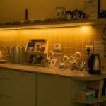 A coffee station with a shelf of tea, an electric kettle, a rack of brochures, and coffee supplies on a kitchen worktop under warm hygge kitchen lighting.