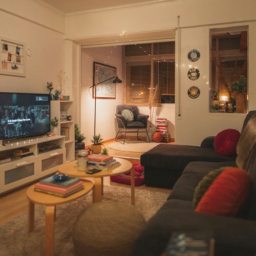 A cosy living room with a dark sofa, two small round coffee tables, a television, and an armchair by a window, highlighted by warm hygge lighting ideas.