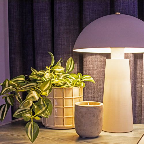 A lit mushroom-shaped table lamp next to a potted plant and a small candle on a surface, offering cosy hygge lighting ideas for a living room.