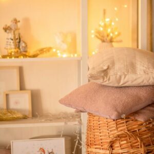Two decorative cushions rest on a woven wicker basket, set against shelves illuminated by hyggelig lighting and candles.